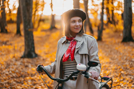 Beautiful dreamy portrait of young smiling woman in french beret cycling alone in park. Sunny day in...