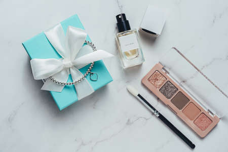 Barcelona, Spain - January 2022. Tiffany and Co gift box with heart bracelet, perfume bottle, eyeshadow palette flat lay top view. Luxury, jewelry cosmetics present on marble backgroundのeditorial素材