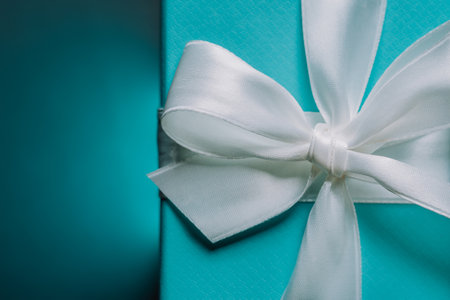 Luxury elegant gift blue box tied with silk ribbon on turquoise background. Birthday present, anniversary, cards, postcards, wallpaper concept.の写真素材