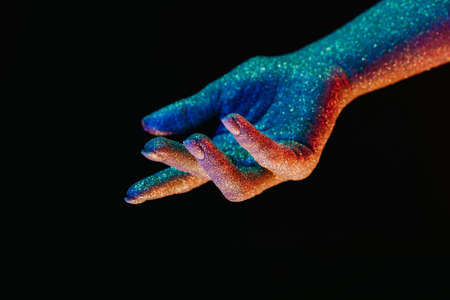 Female hand covered with holographic shining glitter under neon colored light. Body art, glamorous conceptual, fashion style.の写真素材