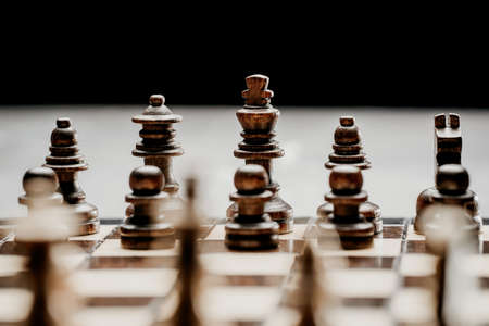 Pieces on chessboard. Board intelligence game - wooden chess on dark background. Business solutions, challenge, sport, success strategy concept.の写真素材