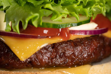 Macro detailed view of juicy beef burger layers. Cutlet, onion, vegetables, melted cheese, lettuce, sauce and topped sesame seeds. Hamburger. Junk fast food concept.の写真素材