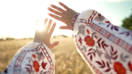 Woman hands touching warm rays, sunset time. Female palm wearing beautiful vyshyvanka - embroidered...