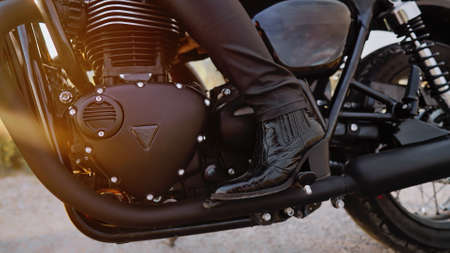 Legs of stylish motorcyclist woman sitting on classic bike. Black retro-styled motorcycle. Details...