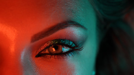Close-up of woman eye under orange blue neon light. Female with beautiful makeup, glitter shadows. Beauty, cosmetics, night club lifestyle concept.の写真素材
