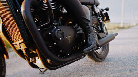 Legs of stylish motorcyclist woman sitting on classic bike. Black retro-styled motorcycle. Details...
