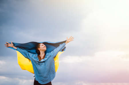 Happy free ukrainian woman with national flag on dramatic sky background. Portrait of lady in blue...