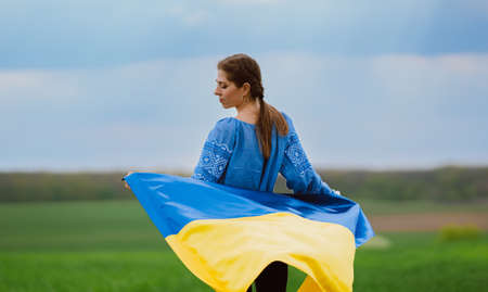Beautiful ukrainian woman with national flag on green field background. Young lady in blue embroidery vyshyvanka. Ukraine, independence, freedom, patriot symbol, victory in war.の写真素材