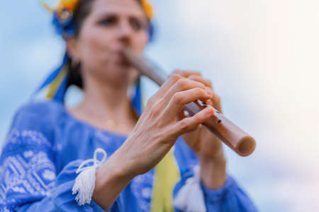 Woman playing woodwind wooden flute - ukrainian sopilka outdoors. Folk music, culture concept. Musical instrument. Lady in traditional embroidered shirt - blue vyshyvanka.の写真素材