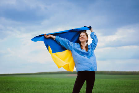 Happy free ukrainian woman with national flag on dramatic sky background. Portrait of lady in blue embroidery vyshyvanka shirt. Ukraine, independence, patriot symbolの写真素材