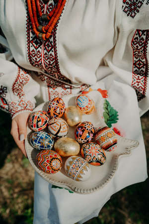 Ukrainian woman holding in hands Easter eggs. Beautiful geometric slavic decoration. Lady in embroidery vyshyvanka dress.の写真素材