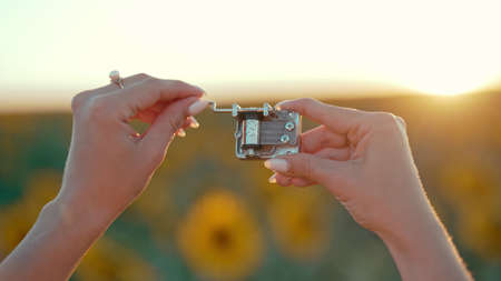 Female hands rotating gears of old music box mechanism. Lady turning the lever of retro small metallic carillon. Woman in sunflowers field listening to music which playing.の写真素材