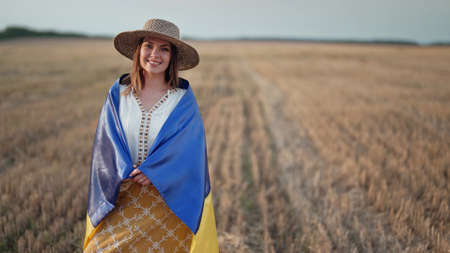 Smiling ukrainian woman with national flag in wheat field after harvesting. Charming rural lady in embroidery vyshyvanka. Ukraine, independence, freedom, patriot symbol, victory in war.の写真素材