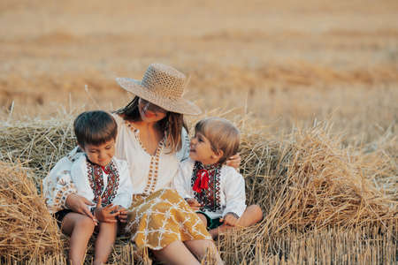 Ukrainian boys and mother sitting together on wheat in field after harvesting. Family, friends holding hands. Children is our future. Happy childhood.の写真素材
