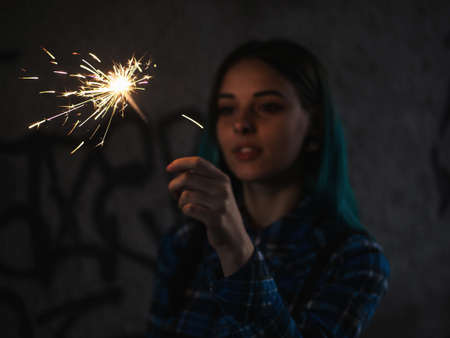 Portrait of model girl with blue hair looks with sparklers in their hands. Close up. Beautiful young teenage in city tunnel having fun with bengal fire.の写真素材