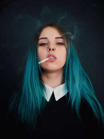 Emo girl smoking cigarette. Young student or pupil with blue colorful dyed hair, hat,...