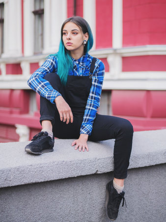 Hipster girl with blue dyed hair. Woman with piercing in nose, ears tunnels and unusual hairstyle having fun, posing in European city. Carefree concept.の写真素材