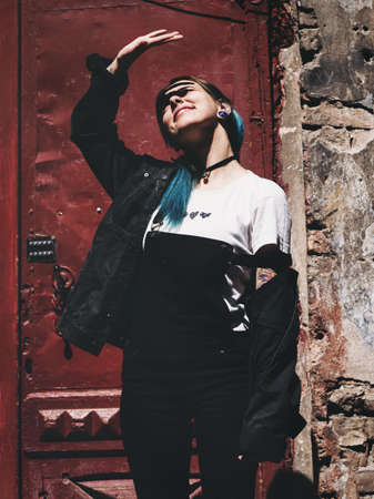 Street punk or hipster girl with blue dyed hair. Woman with piercing in nose, violet lenses, ears...