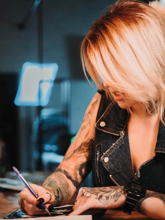 Tattoo artist drawing illustration of skull inside ink studio. Woman with black nails and rings at work. New fashion lifestyle artistic trends concept . Warm cinematic filter.の写真素材