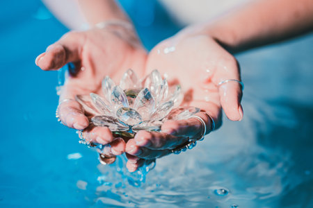 Woman holding fragile lotus flower. Clean water drops are dripping from crystal. Concept of religion, kundalini, meditation, chakras, spiritual inner worldの写真素材
