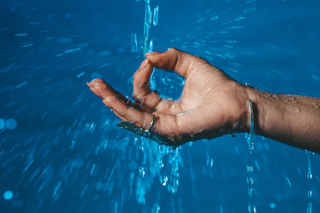 Hand of woman in mudra om under rain or waterfall, meditating in summer. Clean water pouring on...