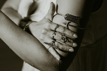 Beautiful gypsy woman demonstrates boho jewelry, rings with turquoise stones on hands. Black and white. Girl in white dress showing accessories in blue water. Femininity, trend, hippie style concept.の写真素材