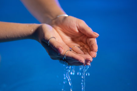 Clean water in woman hands. Palms with gypsy boho rings holding clear aqua. Freshness, purity, life-giving force, tropical background.の写真素材