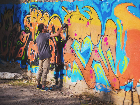 Creative art - teenage boy painting colorful abstract ornament graffiti on street wall with aerosol spray. Back view, overall planの写真素材