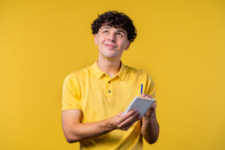 Curly man writing notes in planner with pen. Student guy writes future plans and to-do list in...