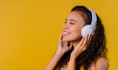 Positive woman listening music, enjoying with headphones on yellow studioの写真素材