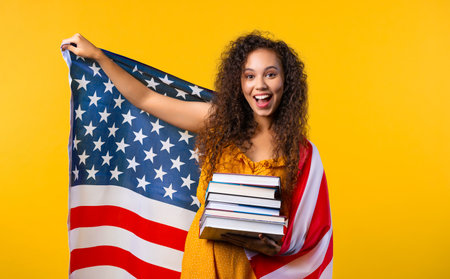 American woman student with stack of books on yellow background.Education in USAの写真素材