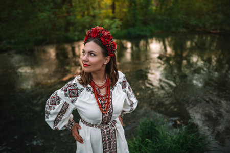 Attractive ukrainian woman in embroidery vyshyvanka, coral beads near riverの写真素材
