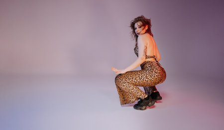 Sexy woman performs flexible movements, twerking body on floor. Seductive hot dance in neon studio. Lady dancer in tight leopard clothes and sneakers. copyspace.の写真素材