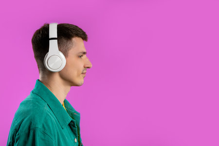 Positive young man listening music, enjoying dance with headphones on violet studio background. Radio, wireless modern sound technology, online player. high qualityの写真素材