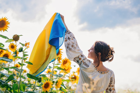 Young ukrainian woman waving national flag on sunflowers, wheat field backgroundの写真素材