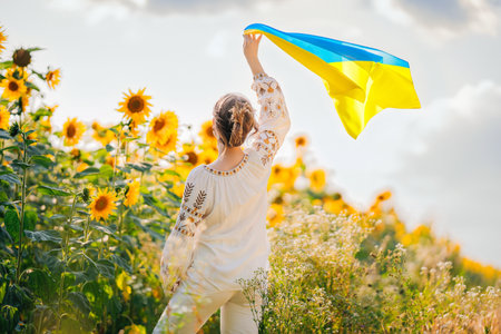 Young ukrainian woman waving national flag on sunflowers, wheat field backgroundの写真素材