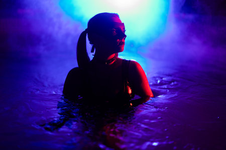 Sensual woman in leather BDSM mask dancing in swimming pool, neon light.の写真素材