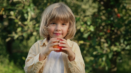 Cute little boy eating, enjoying red tasty apple in garden. Organic fruits, homeの写真素材