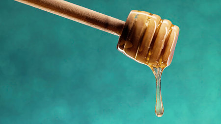 Organic honey flows from wooden dipper stick on blue background. Apiary