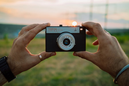 Kyiv, Ukraine - May 2023. Old metal Smena 8 in man hands on sunset background. Soviet manual analog...