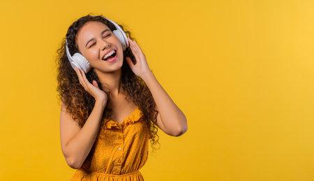 Positive woman listening music, enjoying with headphones, yellow background