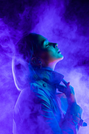 Young woman in neon multi-colors light on smoke, steaming background. stylish