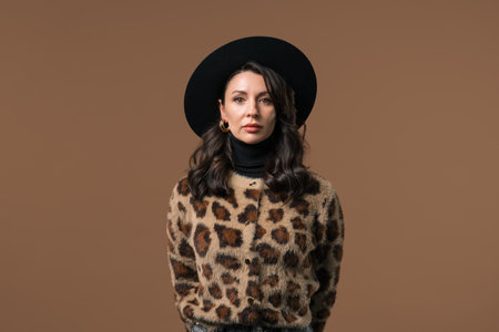 Portrait of 40s european brunette woman in stylish leopard print wear and hat on beige background. Attractive lady. Beautiful make-up, hairstyle, healthy skin.の写真素材