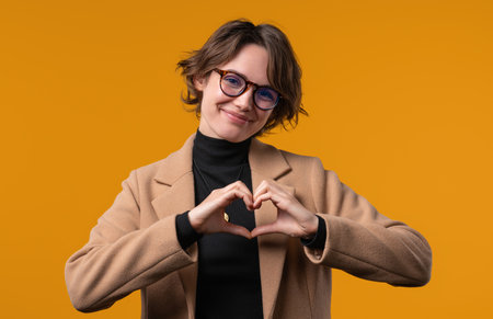Smiling woman showing sign of shape heart. Positive lady on yellow. Love. Women health, volunteering, charity donation, gratitude symbol, flirting conceptの写真素材