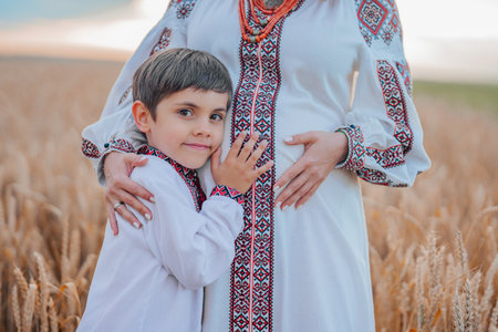 Pregnant Ukrainian Mom With Son In Wheat Field, On Nature. Happy Smiling Boy Brother Touching mothers bump tummy.の写真素材