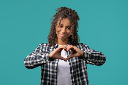 Smiling african american woman showing sign of shape heart. Positive teenager girl on blue. Love....