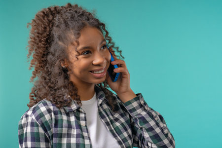 Attractive African american woman talking by phone, smiling. Young teenager girl on blue backgroundの写真素材