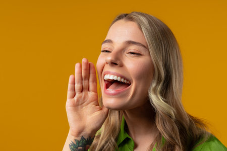 Attention, portrait of blonde young woman shouting, holding hand near open mouth