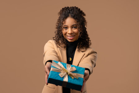 Happy african woman gift box on beige background. Young girl smiling, gives youの写真素材