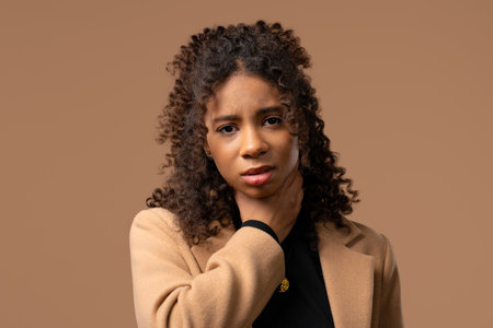 African teenage girl has sore. Woman with swollen throat on beige studio. Anginaの写真素材
